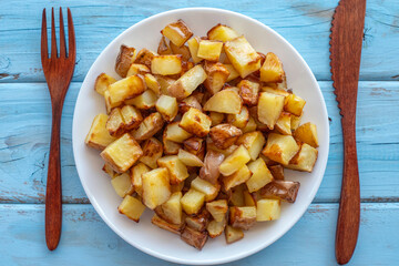 Roasted potato cubes on ceramic plate over wooden background. Top view.
