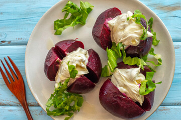 Baked beetroot filled with yoghurt and tahini on ceramic plate over wooden background. Top view.
