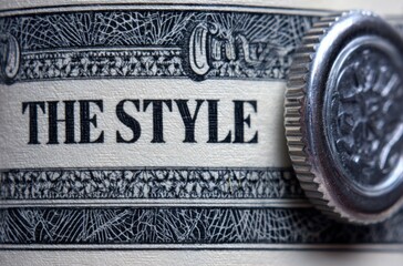 Close-up of a watch crown pressing into patterned paper with the words "THE STYLE" visible, showcasing details and textured surfaces