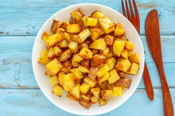 Roasted potato cubes on ceramic plate over wooden background.