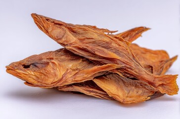 Three whole, dried fish, stacked. They are golden brown and wrinkled, against a white background. The fins and tail are visible on the top fish