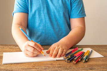 Child holding pencil in the hand on the background of the desk with blank notebook paper.
