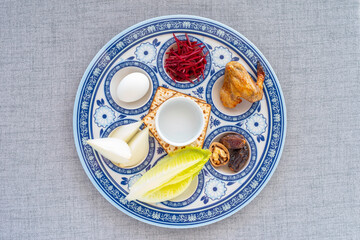 Traditional Seder Plate with symbolic food for Jewish holiday Pesach or Passover over cotton fabric background. Top view.
