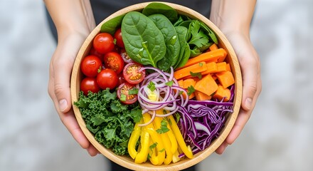 Hands holding a bowl filled with colorful vegetables, top view.