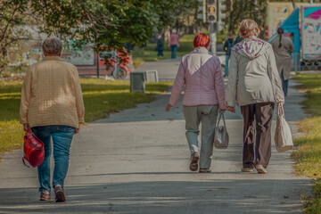 Women with bags walk along the sidewalk on an autumn day