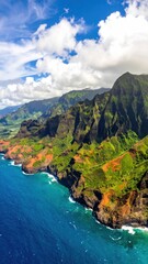 Obraz premium Vibrant coastal landscape featuring jagged cliffs meeting the blue sea under a partly cloudy sky, lush green mountains extend inland