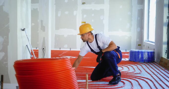 Professional worker inspecting underfloor heating pipes after successful installation, checking if tubes are properly fixed to the floor. Installation of plumbing pipes.