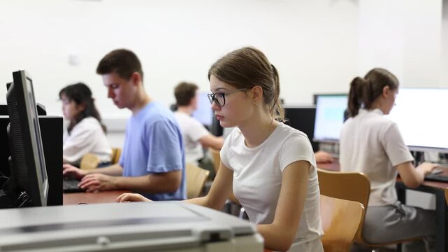  Focused female student in glasses using PC and studying computer science in the classroom