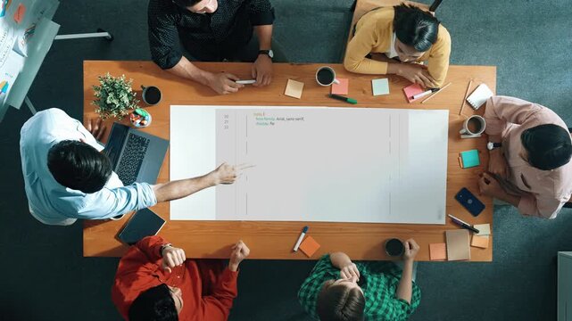 A diverse group of professionals engages in a brainstorming session, surrounded by laptops and notes, fostering creativity and collaboration for effective project planning. Raster