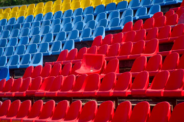 Fototapeta premium Empty red, blue and yellow plastic stadium seats in rows, with one broken chair showing signs of vandalism after a match. Photo