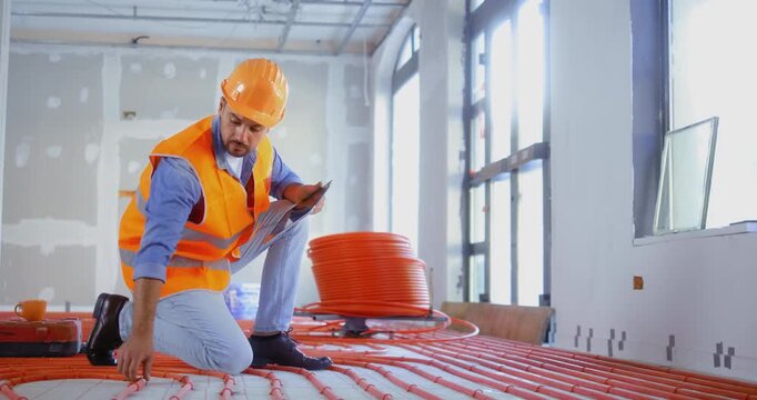 Construction inspector checking a building site using a digital tablet to control the quality of an underfloor heating installation indoors.