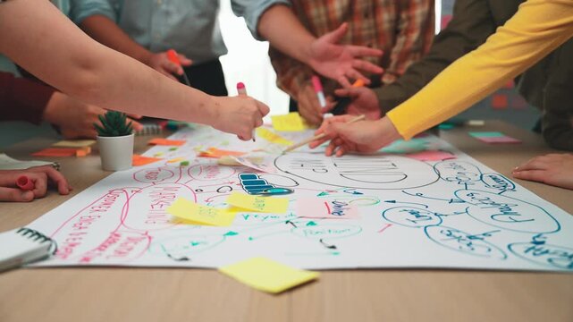 A vibrant scene of a diverse group engaged in a creative workshop, showcasing collaboration through brainstorming ideas on a large paper sheet filled with colorful notes. SACTR - Powered by Adobe