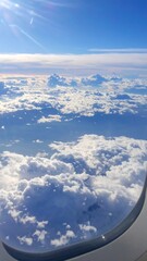 Airplane window view of fluffy white clouds and blue sky with sun rays