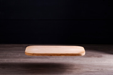 A brown wooden cutting board or board floats on the floor in an atmospheric light coming from the side, dark background, light reflecting on the floor.