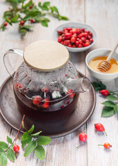 Steaming rosehip tea brewing in glass teapot with honey and fresh rose hips