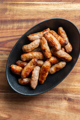 Cooked party cocktail sausages in a black stoneware dish background backdrop. Acacia wood chopping board background.