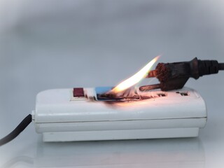 The image depicts an electrical fire originating from an overloaded or faulty power strip and plug.