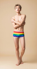 A confident young man posing in rainbow shorts against a neutral background. The image highlights fashion, youthful style, and body confidence.