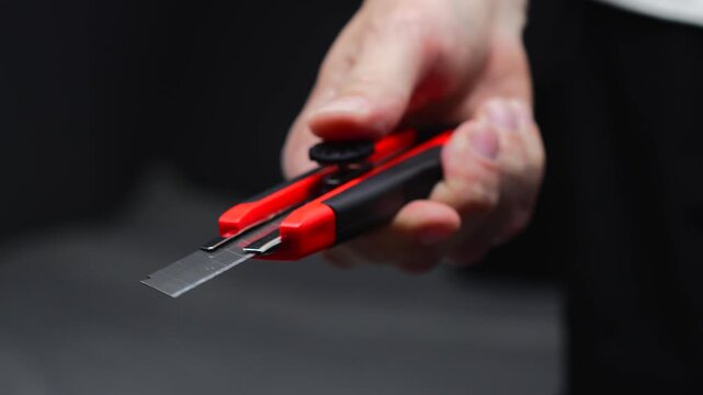 A man extends the blade of a sharp paper cutter.
A close-up of a utility knife in his hands.
A mechanical cutter for construction work or an office paper cutter.