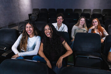 Group of young friends laughing and enjoying a comedy film together at the cinema, sharing joyful moments in a relaxed atmosphere