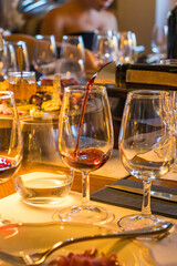 Close-up of a red wine glass on a dinner table with gourmet snacks, cheese, charcuterie, and appetizers. Warm evening atmosphere with elegant lighting, people in background, and luxury dining setting