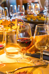 Close-up of a red wine glass on a dinner table with gourmet snacks, cheese, charcuterie, and appetizers. Warm evening atmosphere with elegant lighting, people in background, and luxury dining setting