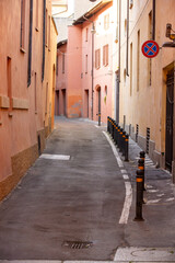 An enchanting, narrow European alleyway, flanked by traditional buildings with warm-toned stucco and closed shutters, creating a feeling of classic, old-world urban life perfect for travel or architec