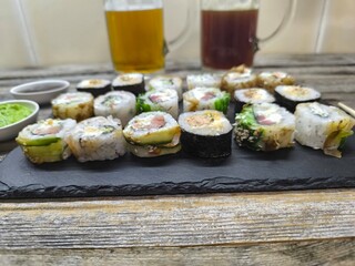 An assortment of typical Japanese dishes - sushi, on a granite board with various sauces. Glasses of light and dark beer stand nearby