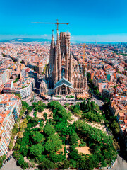 Aerial view of Barcelona with the Sagrada Familia, city buildings, park, and sea skyline in the distance on a sunny day.
