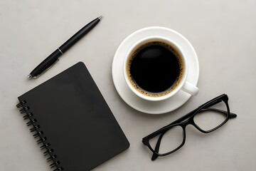 A top-down view of a work desk with a hot cup of black coffee, a black pen, a spiral notebook, and a pair of eyeglasses.