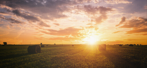 Sunset over hay bales in a field. Golden light bathes the landscape, creating a tranquil scene. For agriculture, travel and inspiring greeting card designs. Vintage film aesthetic. © Eugene_Photo