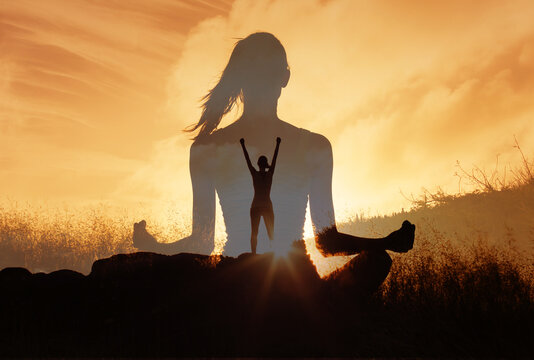 Silhouetted woman sits meditating in a peaceful landscape at sunset, image of an empowered person raising arms on a mountain top. Evokes strength, calm, and inner strength growth.