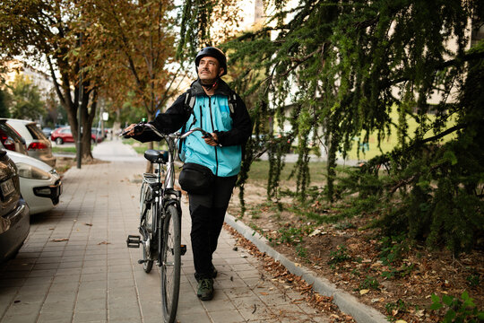 Delivery man walking with bicycle and checking his smartphone