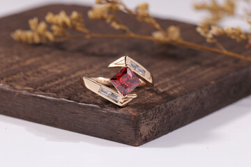 Close-up of a unique gold ring with a red gemstone and artistic design, set on a wooden surface, symbolizing luxury and fine jewelry.