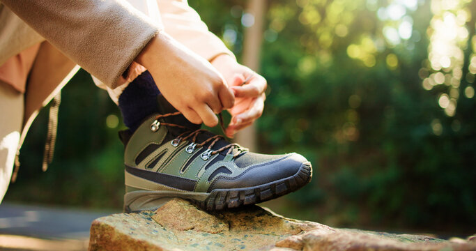 Person, hands and tying shoes on rock for hiking preparation, trail or path in outdoor forest. Closeup, hiker or getting ready with tie, laces or boots for travel, trekking start or walk in nature
