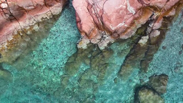 An abstract aerial video of crystal clear turquoise water with the red rocky sea bed visible below creating a beautiful and mesmerizing natural pattern with light reflections