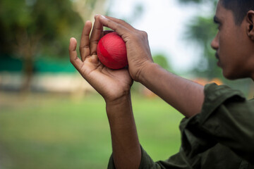 A young boy holding a red cricket ball, preparing to bowl