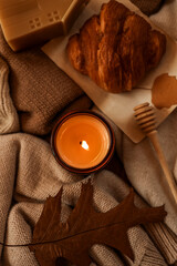 Cozy autumn still life with a lit candle, croissant, and fall leaf.