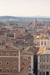Obraz premium An elevated, panoramic view of Rome's historic center, showcasing a dense array of terracotta rooftops, bell towers, and classical domes under a soft, hazy light. Excellent for travel websites, cultur