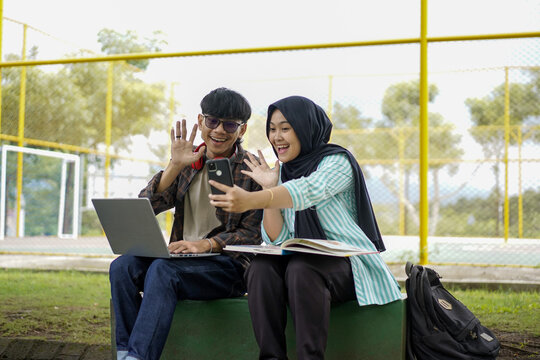 Joyful young students waving during an outdoor video call, showcasing modern campus life and digital connection. A happy moment of remote interaction and shared experience on a sunny day - Powered by Adobe