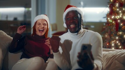 Funny loving couple using video conference in smartphone in Christmas night. Young adult multi ethnic people chatting online by video call with friends, portrait of Caucasian woman and African man - Powered by Adobe