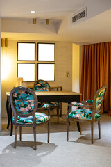 A room with a table and four chairs, all of which are brightly colored. Blank frames for custom content on the wall.