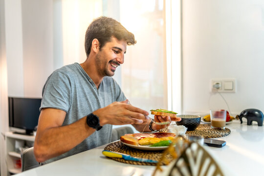 Happy man eating avocado toast for breakfast at home