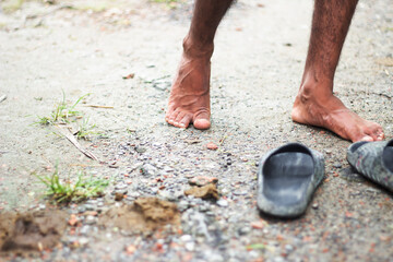 Barefoot person standing on a dirt path with sandals nearby