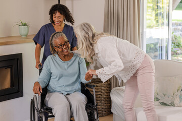 Fototapeta premium Caregiver assisting senior woman in wheelchair while friend visits at home