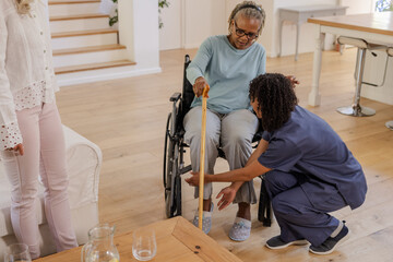 Assisting senior woman in wheelchair, African American nurse helps with walking stick