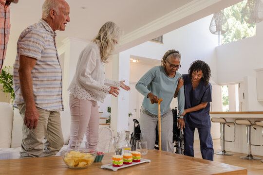Senior friends enjoying time together at home with caregiver assisting