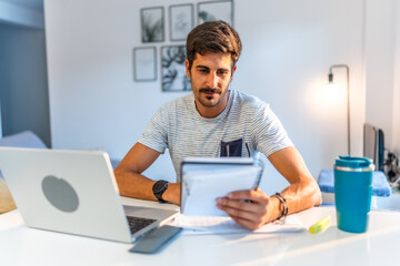 Focused freelancer reading notes and working on laptop at home office