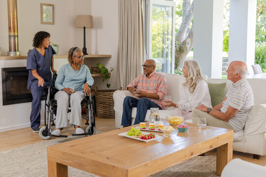 Senior friends enjoying conversation and snacks in cozy living room with caregiver