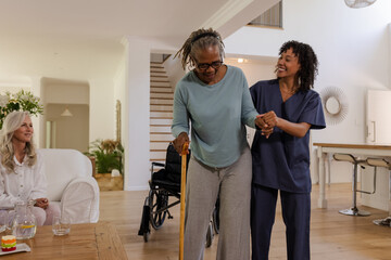 Fototapeta premium African American woman using cane walking with caregiver at home, smiling together
